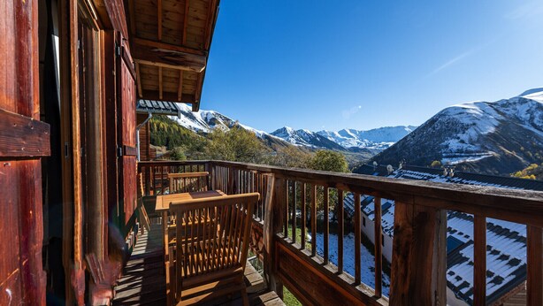 Un balcón de madera con vistas a montañas nevadas y un valle.
