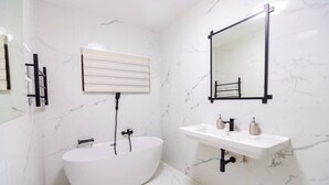 Een moderne badkamer met een vrijstaand bad, een wastafel met spiegel en een handdoekrek.