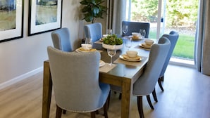 A dining area with a wooden table, six chairs, and a potted plant. - New 4B Home / Sequoia, EV, +More (Visalia)