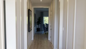A hallway with a wooden bench, white walls, and a door leading to a room. - New 4B Home / Sequoia, EV, +More (Visalia)