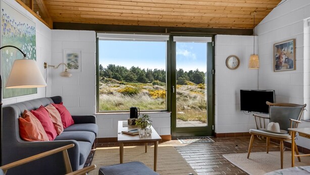 A modern living room with a sofa, coffee table, and chairs. A large window offers a view of a forested landscape. - "Ehawee" - 350m from the sea by Interhome (Saltum)