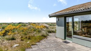 A modern building with a glass door and windows, situated on a stone pathway with a view of a grassy landscape and distant hills. - "Ehawee" - 350m from the sea by Interhome (Saltum)