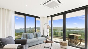 Una sala de estar moderna con un sofá gris, una mesa de centro y vistas a un lago y montañas a través de amplios ventanales.