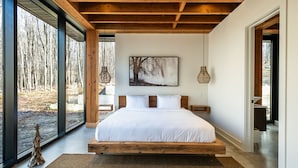Un dormitorio con una cama grande, vigas de madera, un cuadro y vistas a árboles.