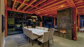 Un comedor moderno con una mesa grande y sillas, una chimenea y un muro de vidrio con vistas al exterior.