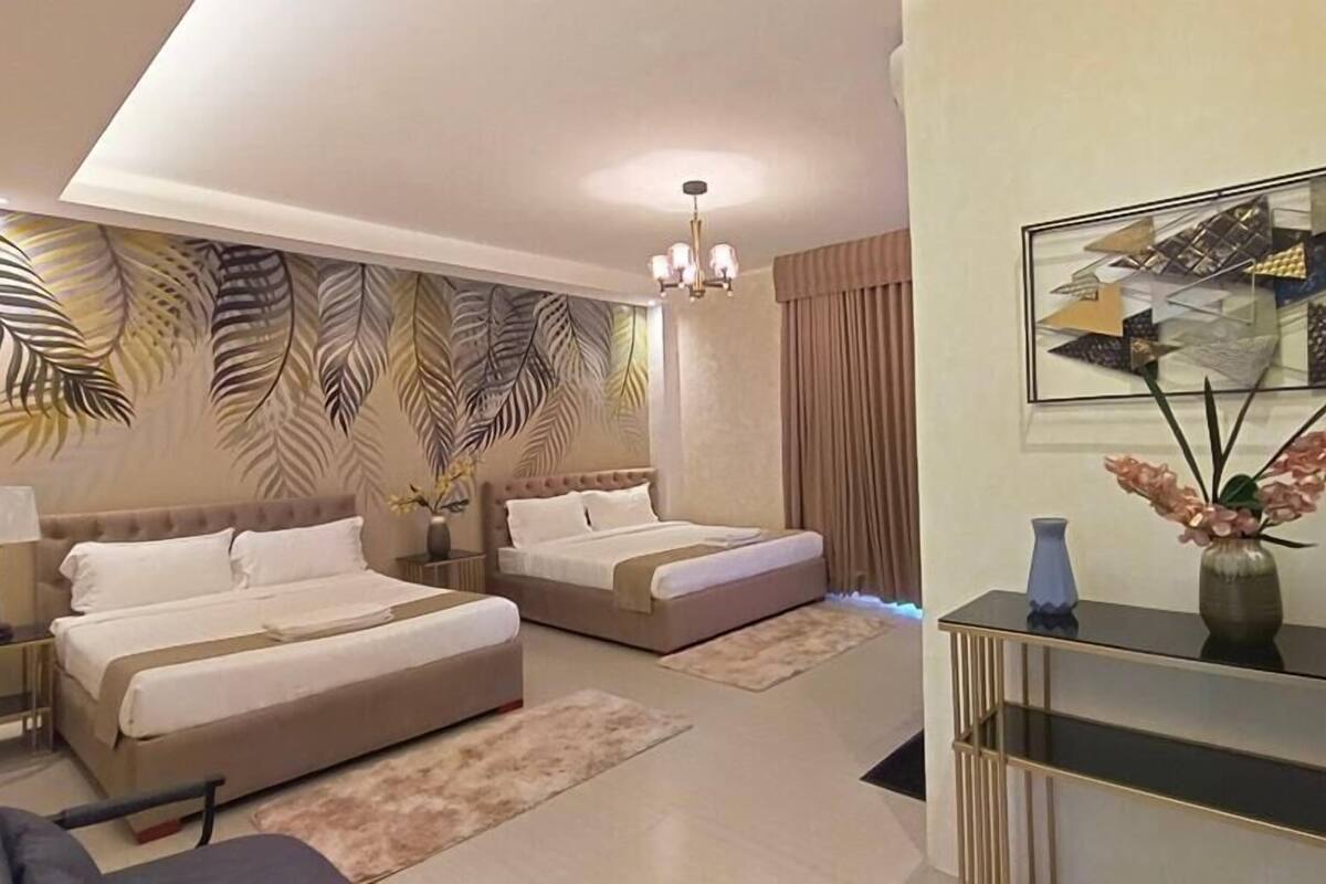 Habitación de hotel con dos camas, un escritorio, una silla, un jarrón con flores y un cuadro en la pared.