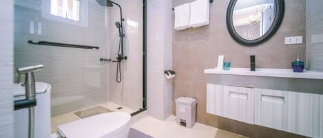 Un baño moderno con ducha de vidrio, bañera blanca, tocador con espejo y un pequeño cesto de basura.