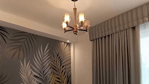Une chambre à coucher moderne avec un grand lit, un lustre, une plante et une vue sur l’extérieur.