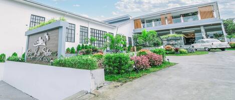 A hotel with a modern design, featuring a large signboard, a well-maintained garden, and a two-story building with a balcony.