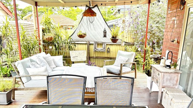 A sunlit patio with glass-top tables, cushioned seating, and hanging plants.