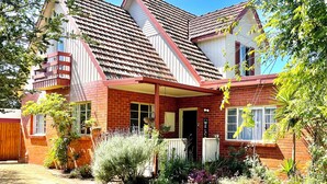 A two-story house with a red brick facade, a balcony, and a well-maintained garden.