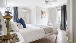 A bedroom with a bed, a ceiling fan, a window with curtains, and a wall-mounted air conditioner.