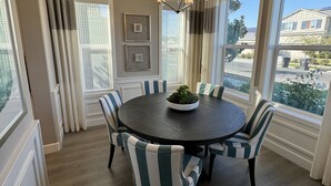 Un comedor con una mesa redonda, sillas a rayas, una araña y ventanas amplias que dan al exterior.