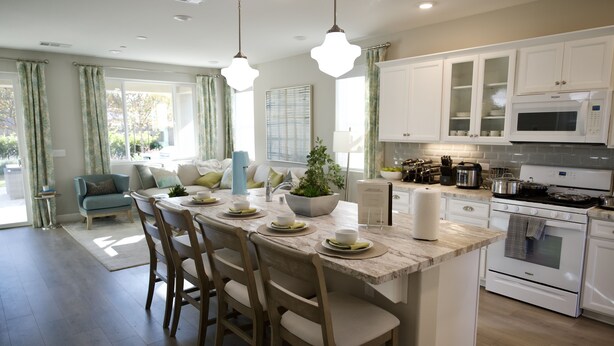 Una cocina moderna con armarios blancos, una isla central con sillas y una zona de comedor con sofá.
