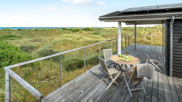 Una terraza de madera con mesa y sillas con vista a un paisaje costero.