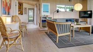 Una sala de estar moderna con techo de madera, televisor, zona de comedor con mesa y sillas, y vista al exterior a través de una ventana.