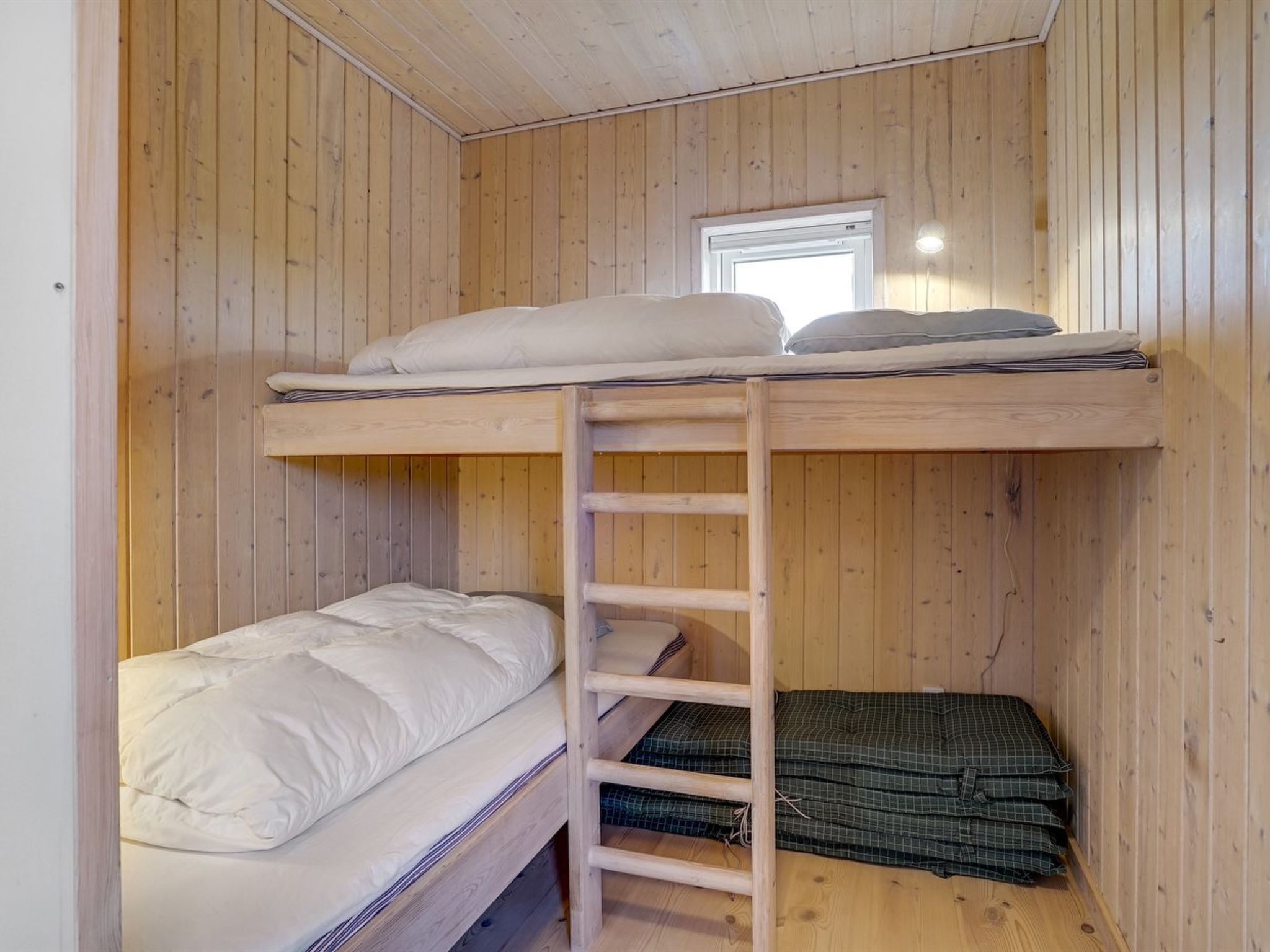 A bunk bed room with wooden walls, a ladder, and a window.