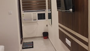 A hallway with a tiled floor, a green mat, a window with blinds, a wall-mounted TV, and a door leading to another room. - Hotel Jayadeep  (Bhubaneshwar)