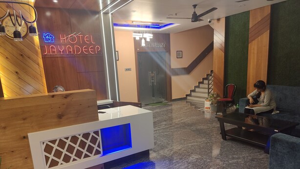 A hotel reception area with a wooden reception desk, a neon sign for 'Hotel Jayadeep', and a staircase leading to the upper floor. - Hotel Jayadeep  (Bhubaneshwar)