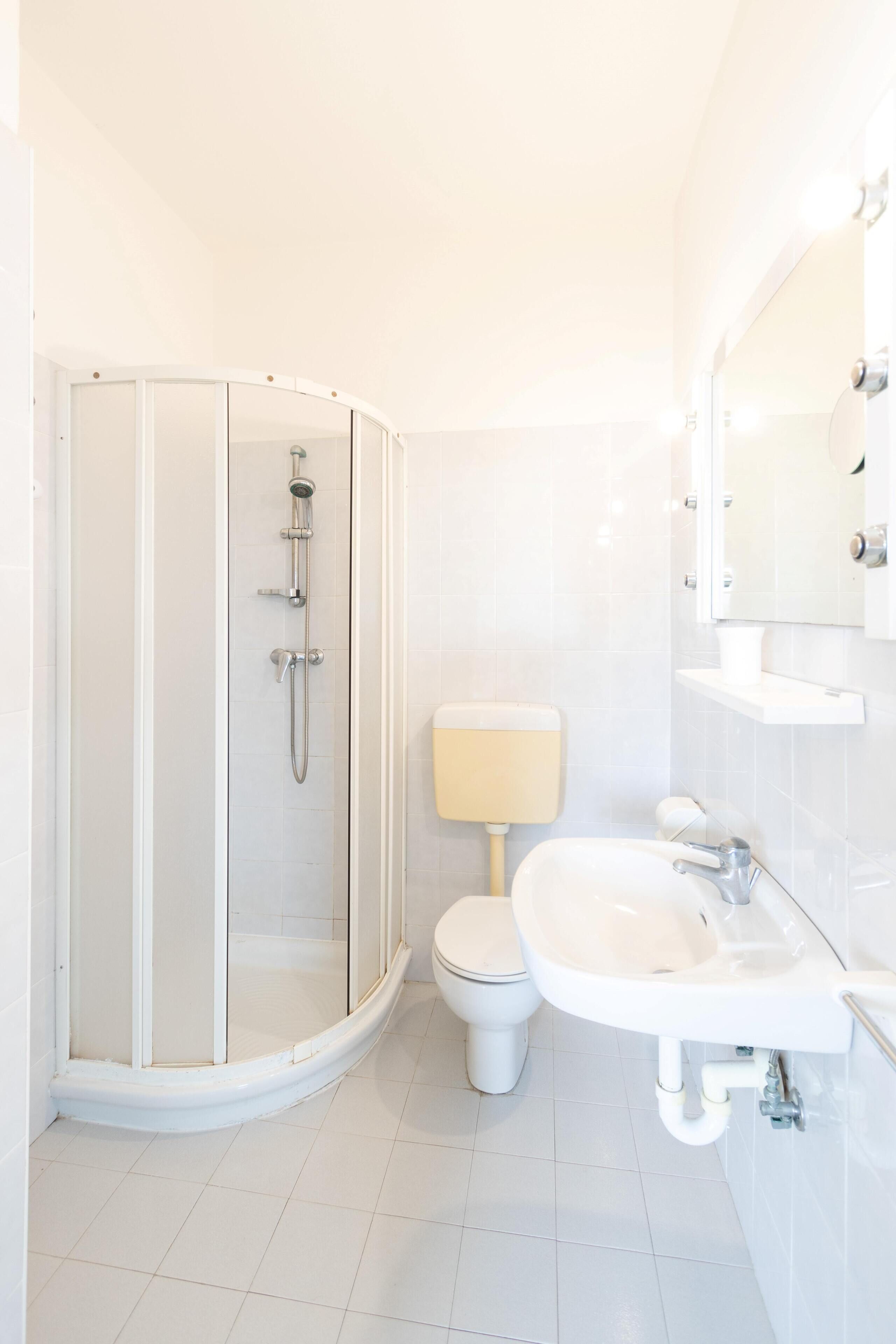 A modern bathroom with a glass-enclosed shower, a toilet, and a sink with a mirror above it.