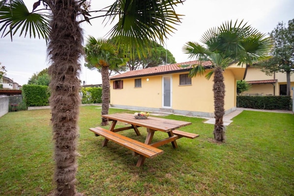 A small yellow building with a tiled roof, surrounded by a grassy lawn and palm trees.