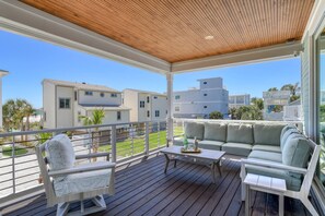 A covered outdoor deck with a wooden ceiling, a sofa, a chair, and a table. - Luxury Home Steps to Beach! 4 Masters, Firepit, Ping Pong, Putting Green, EV charger, Balconies (Saint Augustine)