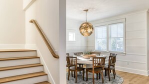 A staircase with wooden steps and a handrail, leading to a dining area with a round table, chairs, and a patterned rug. - Luxury Home Steps to Beach! 4 Masters, Firepit, Ping Pong, Putting Green, EV charger, Balconies (Saint Augustine)