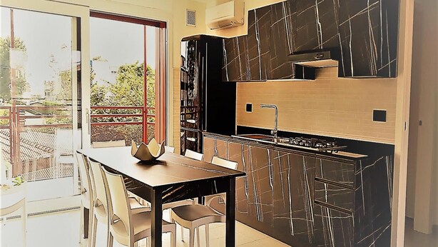 A modern kitchen with a black marble backsplash, a built-in stove, and a dining area with a table and chairs. - Stunning Villa-beahost (Lignano Sabbiadoro)