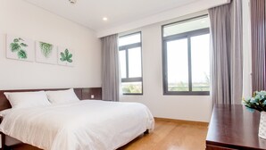 A bedroom with a large bed, wooden flooring, and a view of the outdoors through two windows. - Garden View 2 bedrooms Ocean Suites (Da Nang)
