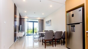 A modern kitchen with a built-in refrigerator, a dining table with chairs, and a view through the glass door to the outside. - Garden View 2 bedrooms Ocean Suites (Da Nang)
