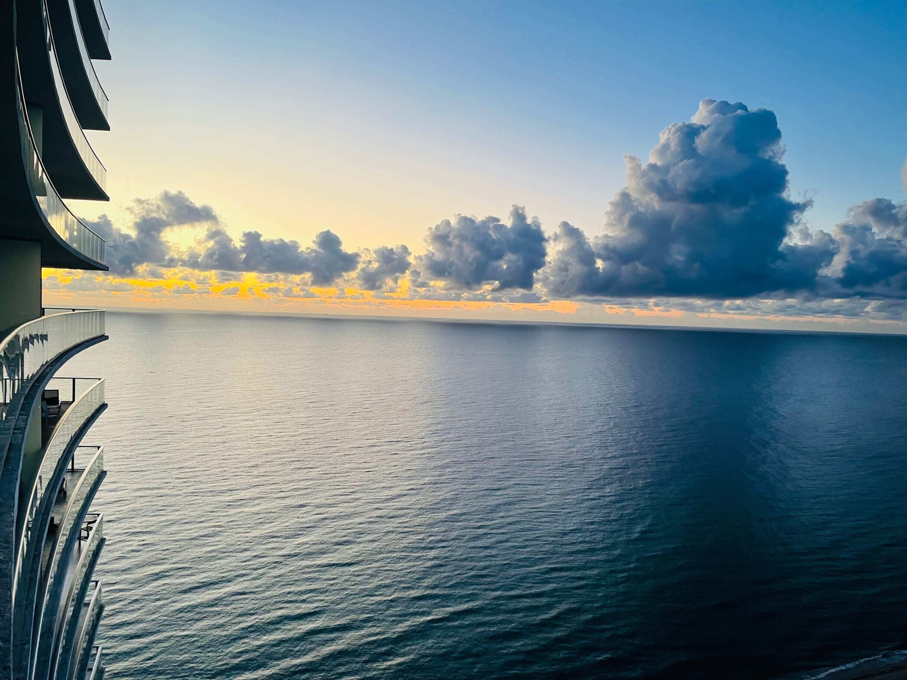 A view from a balcony overlooking a calm sea with a clear horizon and clouds in the sky.