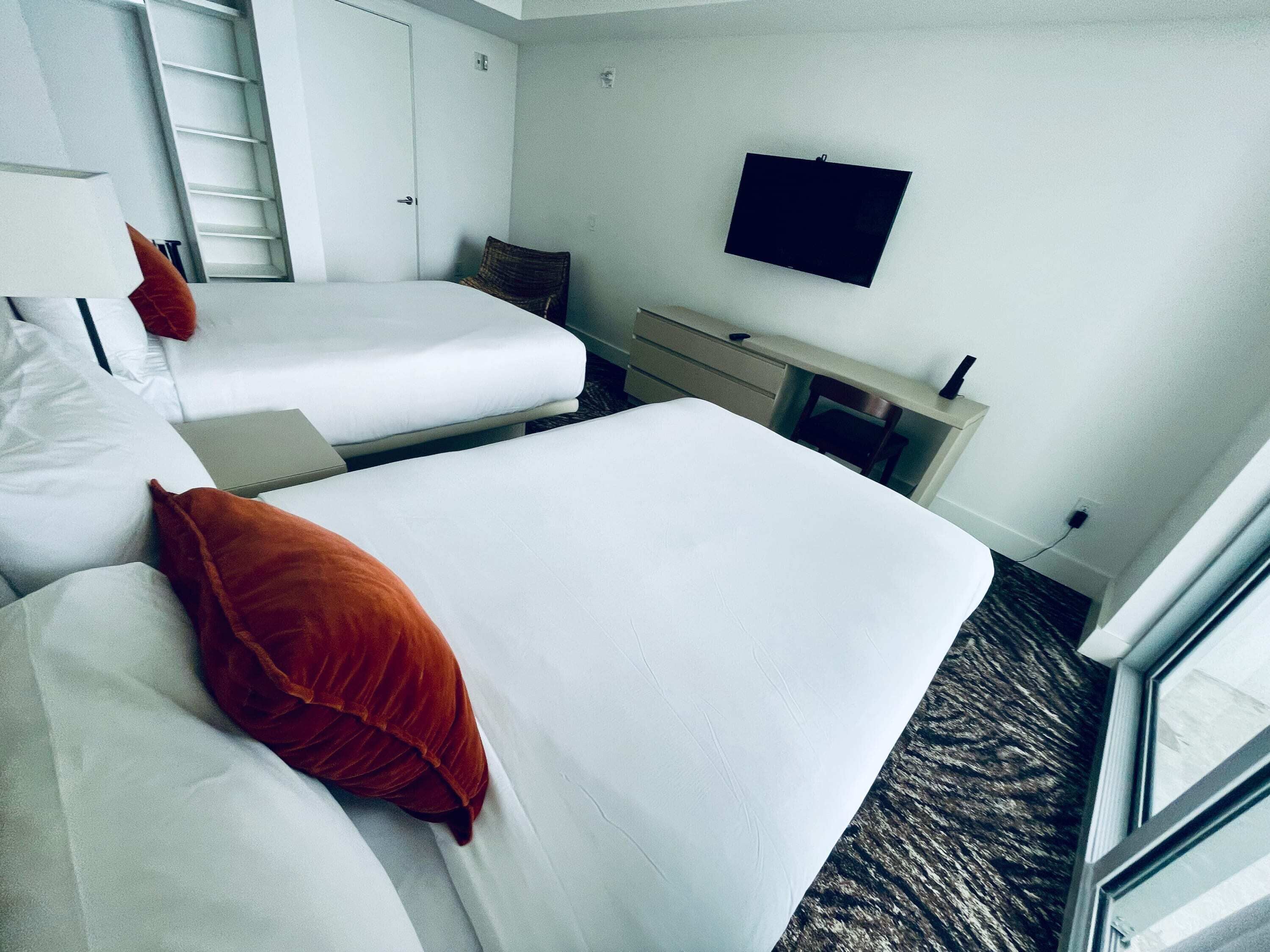 Habitación de hotel con dos camas, un escritorio, una silla, un televisor y una ventana.