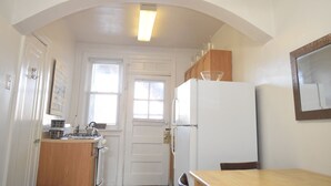 A compact kitchen with a white refrigerator, wooden cabinets, a small sink, and a window. - 6647 1W | Quaint Studio in Central St. Louis (St. Louis)