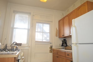 Une cuisine avec des meubles de rangement en bois, un réfrigérateur blanc, une cuisinière et une fenêtre avec des stores.