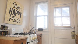 A kitchen with a stove, oven, and a window with blinds. There's a sign on the wall that says "Our Happy Place". - 6647 1W | Quaint Studio in Central St. Louis (St. Louis)