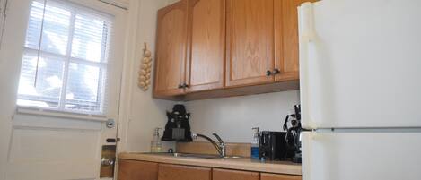 A kitchen with wooden cabinets, a white refrigerator, a sink, and a window with blinds.