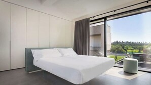 Un dormitorio moderno con una cama grande, vistas a un paisaje urbano y un balcón.
