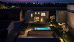Una casa moderna de dos pisos con piscina, rodeada de un césped cuidado y vista al mar al atardecer.