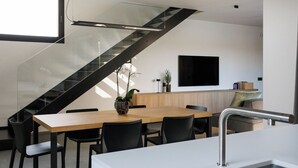 Una cocina moderna con una mesa de comedor de madera, sillas negras, una encimera blanca y una escalera negra.