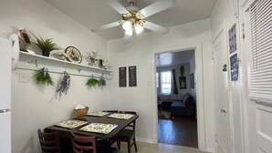 A dining area with a ceiling fan, wooden chairs, a table with placemats, and wall-mounted shelves with plants and decorative items. - 6653 1N | European Style Unit Near Forest Park (St. Louis)