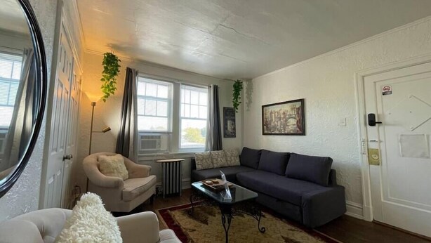 A living room with a beige sofa, a dark grey sofa, a glass coffee table, and a red and brown patterned rug. - 6653 1N | European Style Unit Near Forest Park (St. Louis)