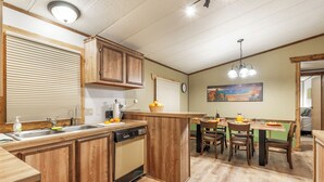 Une cuisine dotée de meubles en bois, d’un lave-vaisselle, d’un évier et d’un coin repas avec des chaises et une table.