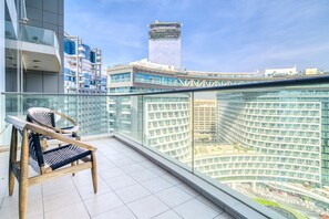 A balcony with a view of a modern building complex, a chair, and a glass railing.