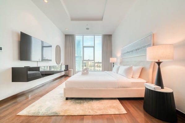 A modern hotel room with a large bed, a flat-screen TV, a side table with a lamp, and a city view through large windows.