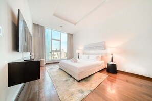 A modern hotel room with a large bed, a flat-screen TV mounted on the wall, a city view through large windows, and a minimalist decor.
