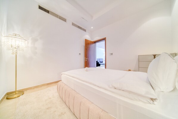 A bedroom with a bed, a bedside table, a lamp, and a door leading to another room.