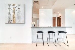 A modern kitchen with a central island, three black bar stools, and a large abstract painting on the wall.