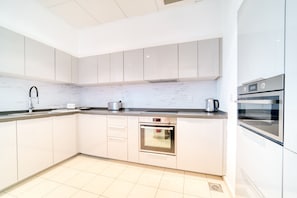 A modern kitchen with white cabinets, stainless steel appliances, and a tiled floor.