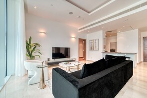 A modern living room with a large black sofa, a TV, and a dining area with a small table and chairs.