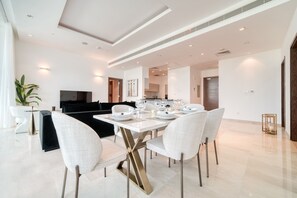 Un espace repas moderne avec une table blanche dressée pour quatre personnes, entourée de chaises blanches.